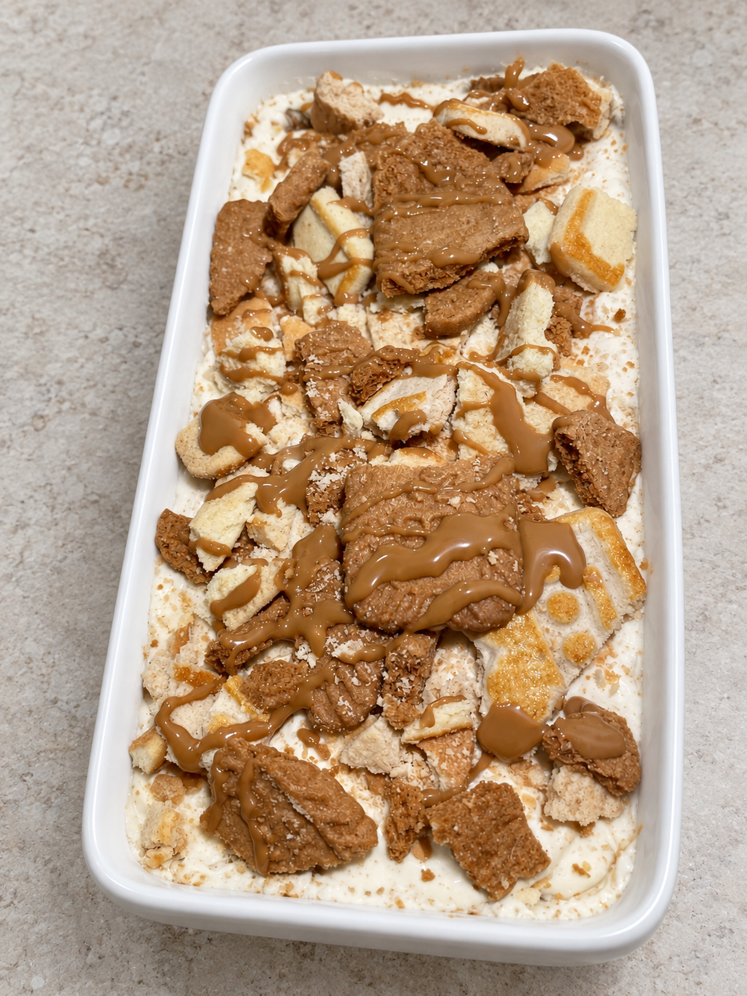 Pudding topped with Biscoff cookies and cookie butter drizzle in a white serving dish