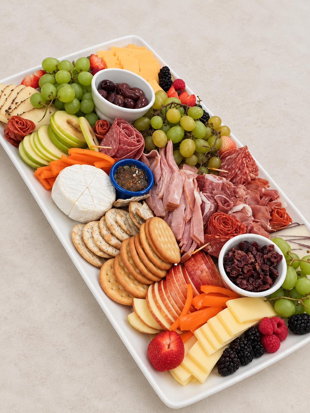 Charcuterie platter with cheeses, meats, fruit, crackers, nuts and olives on a white ceramic platter