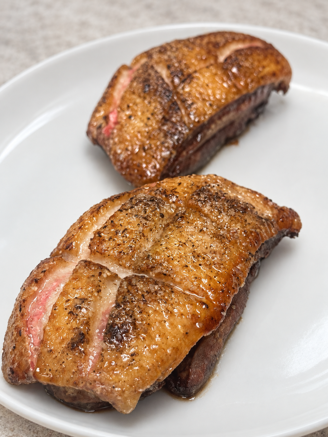 Two roasted duck breasts with crisp golden skin on a white plate