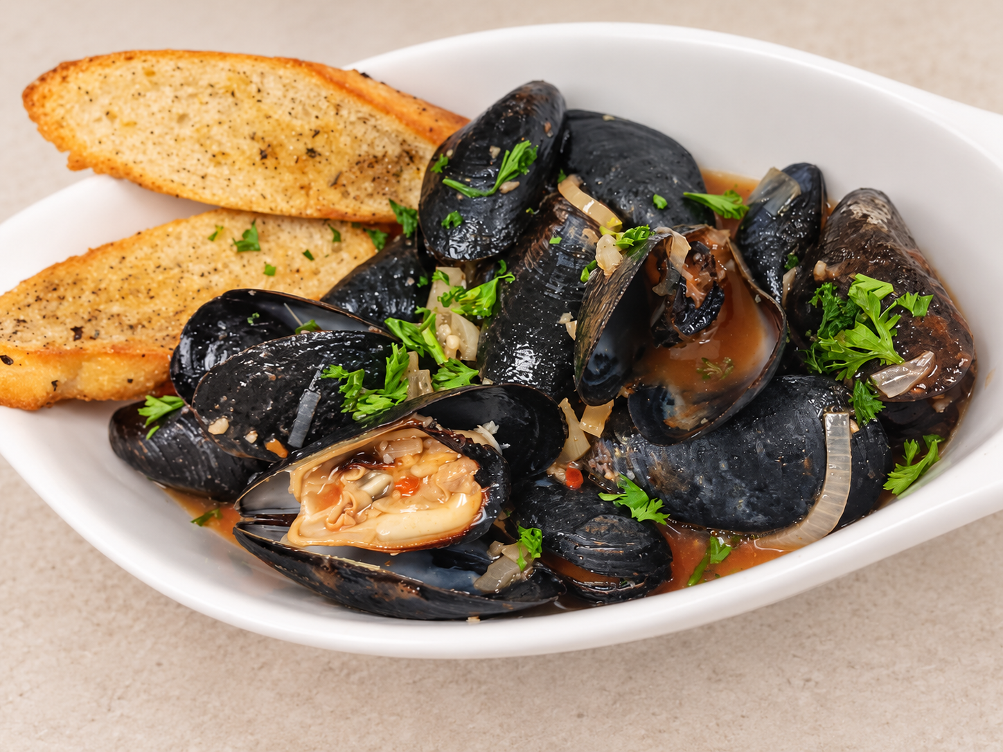 Garlic-herb mussels in broth with toasted bread in a white ceramic bowl