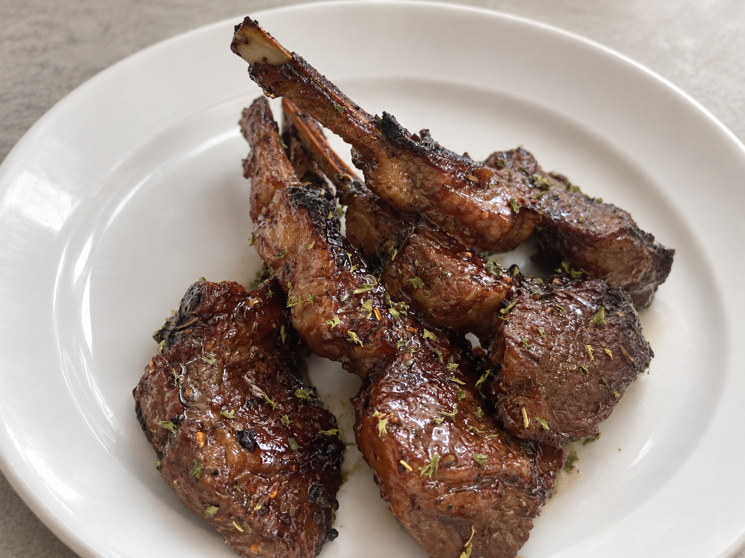 Glazed and seasoned lamb chops arranged on a white ceramic plate