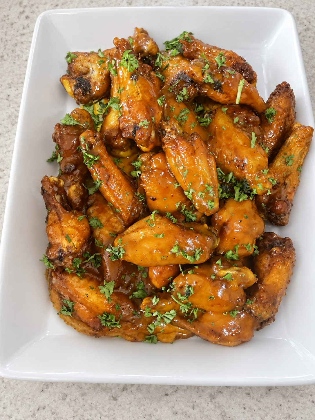 Glossy sauced chicken wings on a white ceramic serving platter